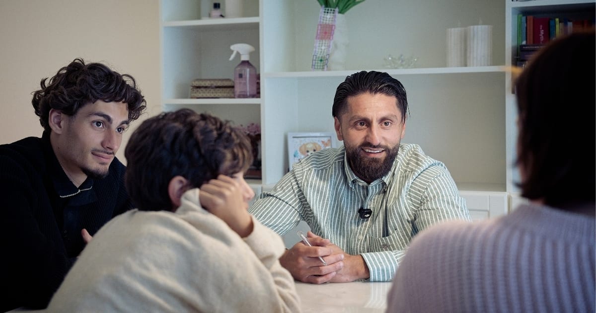 Mentor og ung mand i samtale med to børn i hjemligt miljø